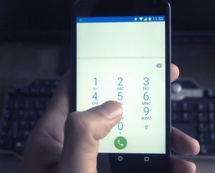 A person is using a smartphone to dial a number, with a keypad displayed on the screen.
