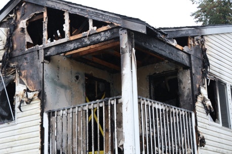 The image shows a building with significant fire damage, including charred walls and a burned balcony area.