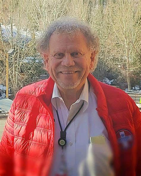 A smiling person in a red jacket with snowy trees in the background.