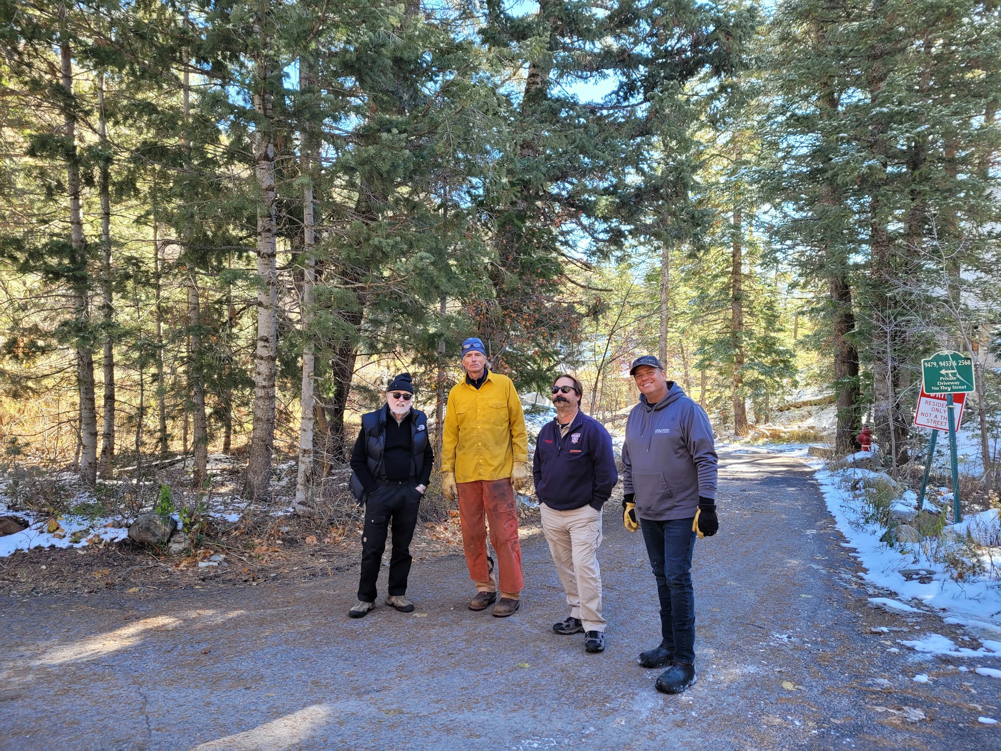 Four people standing on a snowy forest road next to a trail sign.