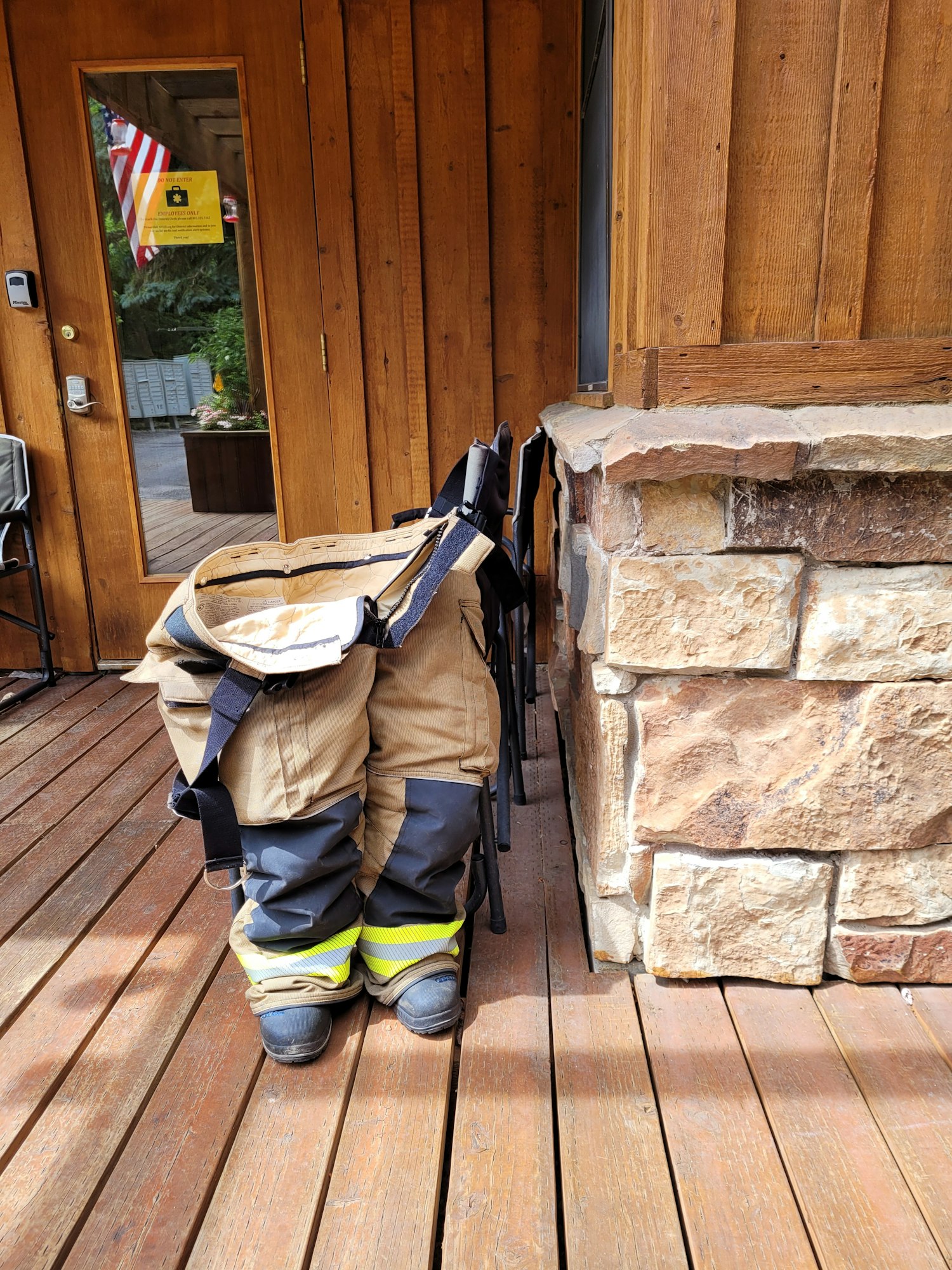 Firefighter uniform and boots on a wooden deck beside a stone wall. Image is rotated 90 degrees.