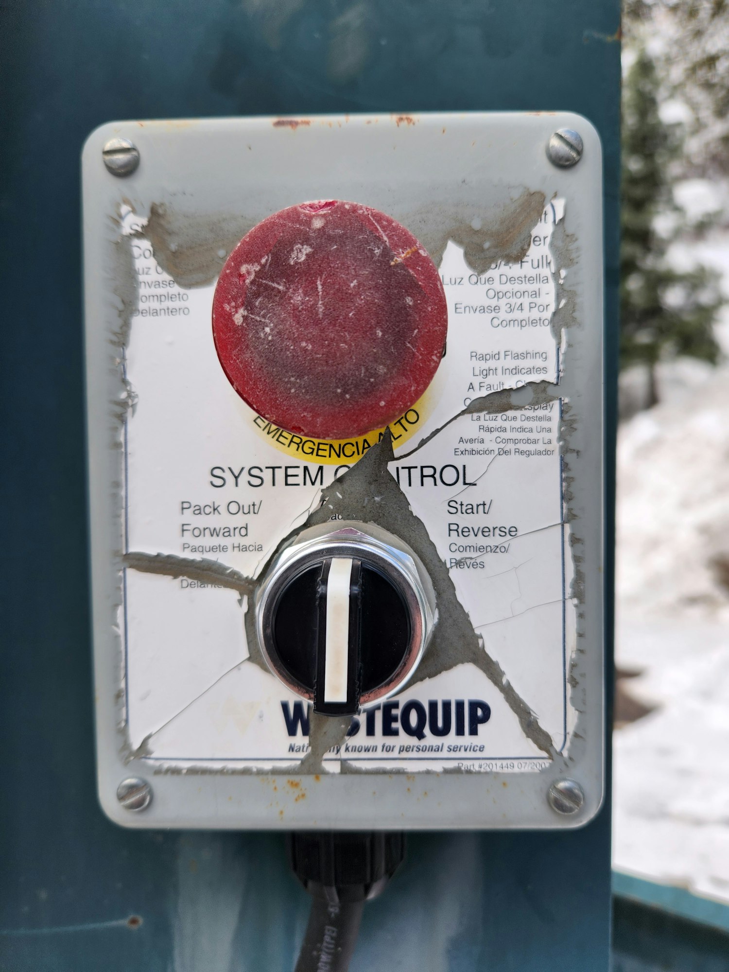 A weathered control panel with a red button, toggle switch, and connector cable.
