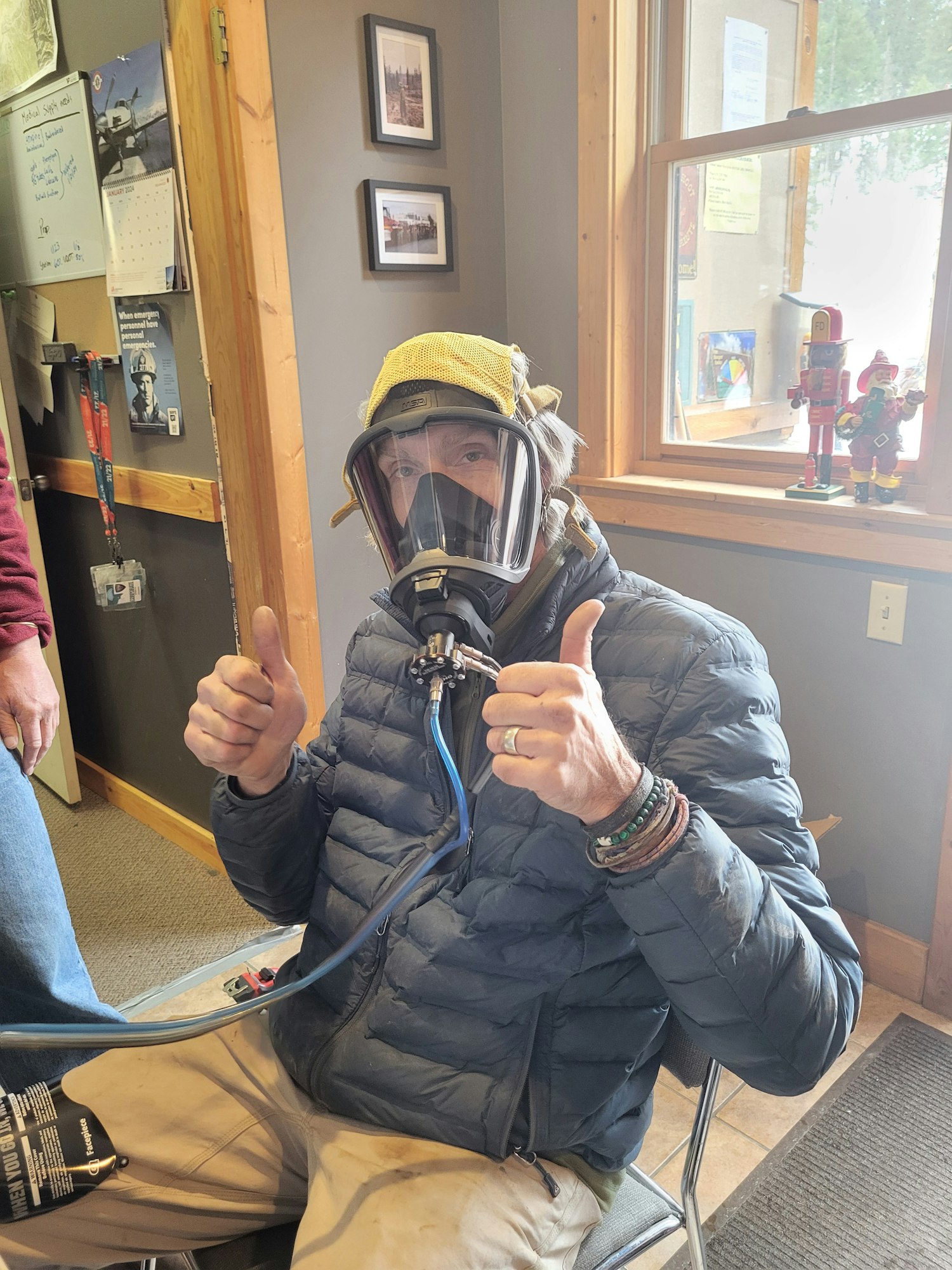 A person wearing a diving mask and holding a thumbs up in a room. (Image is rotated)
