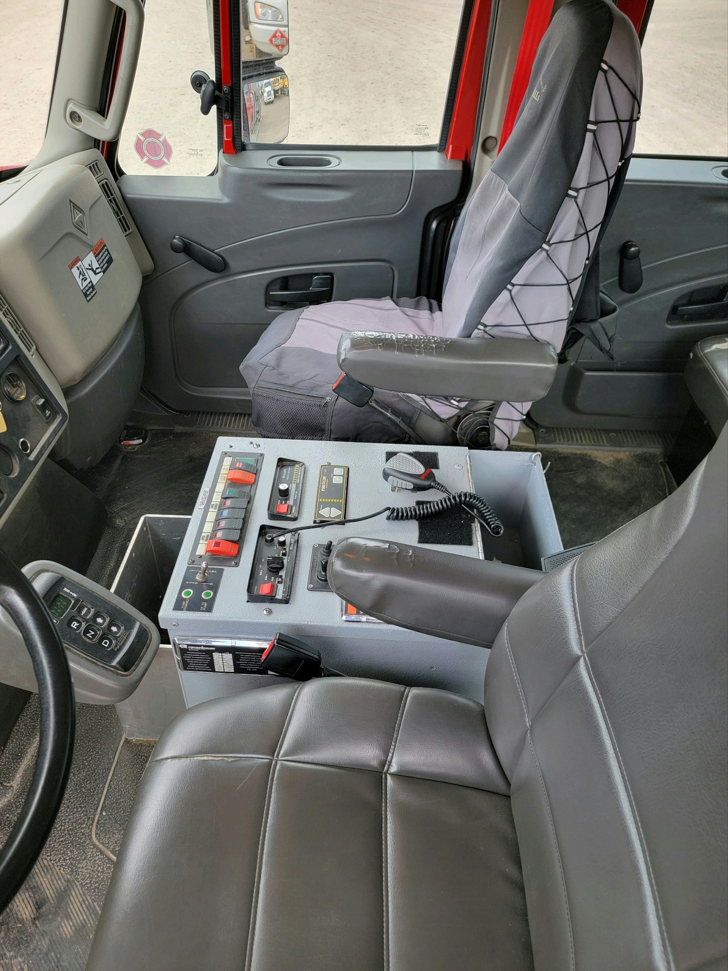 Cab interior with control panel, seats, steering wheel, and door view including a rearview mirror.