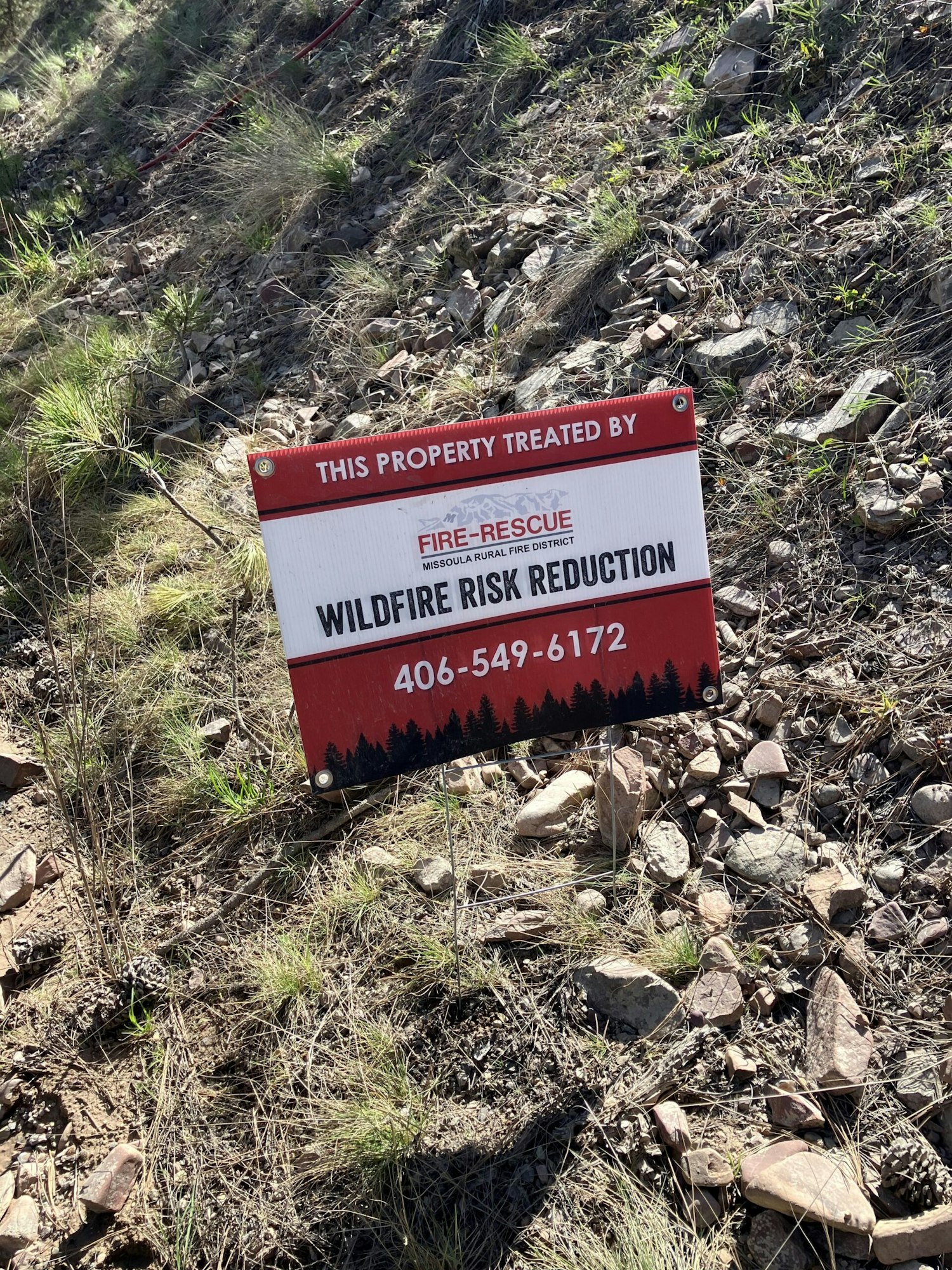 A sign for wildfire risk reduction by Missoula Rural Fire District, placed on rocky ground.