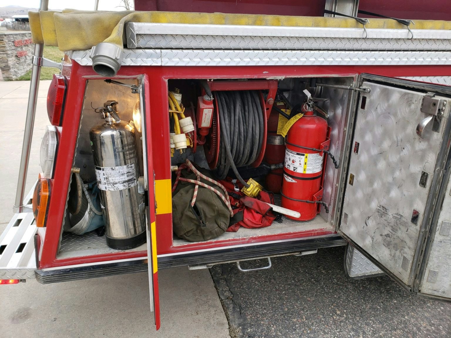 Open fire truck compartment with extinguishers, hoses, and safety equipment.