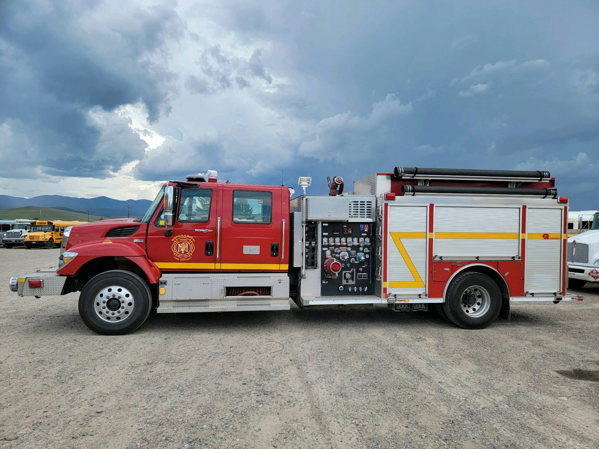 A red fire truck parked on a gravel surface under a cloudy sky.