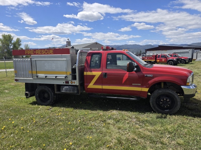 A red fire-rescue truck equipped for emergency response, parked in a grassy area under a blue sky with clouds.