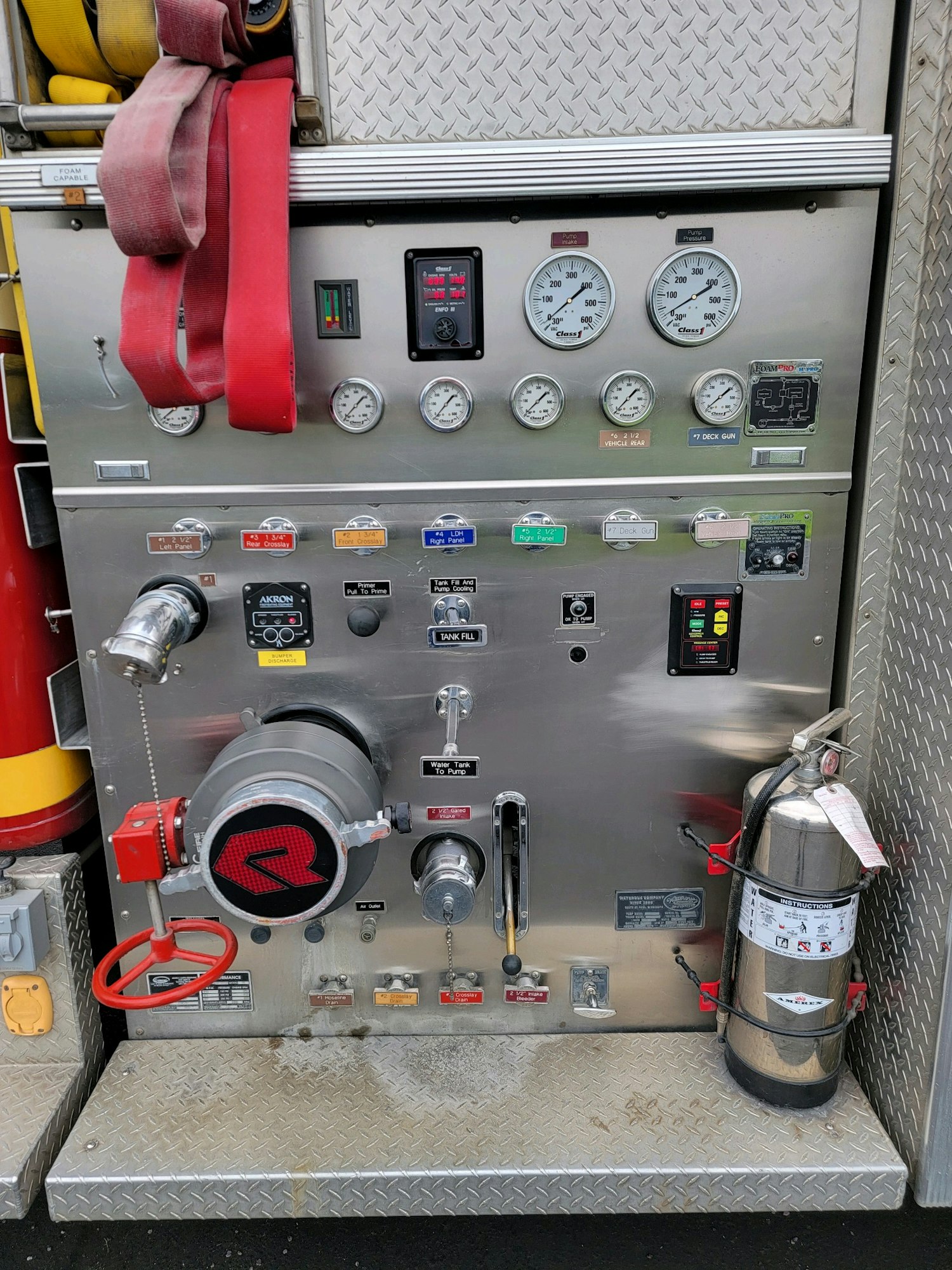 Fire truck control panel with gauges, hoses, and a fire extinguisher.