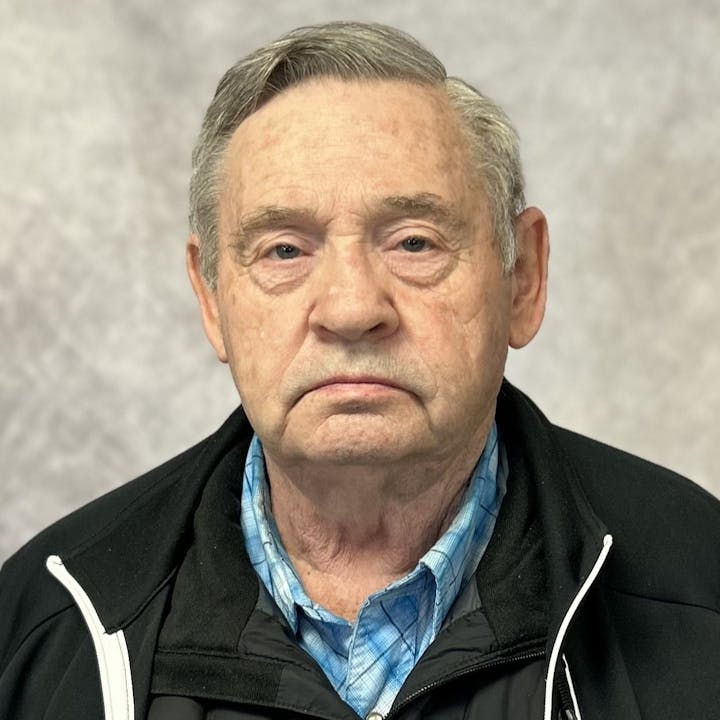 A man wearing a black jacket against a gray background
