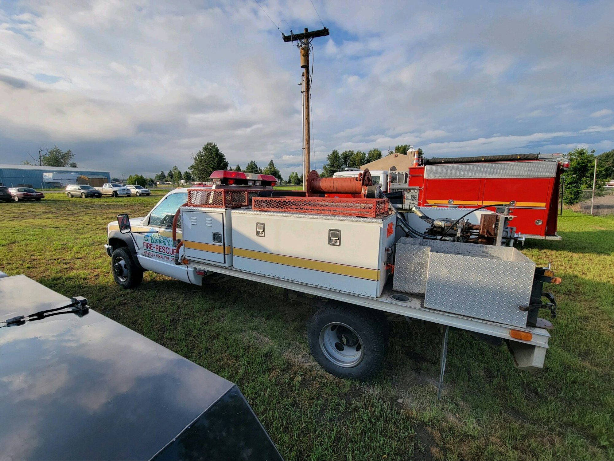 A fire rescue truck parked on grass near other vehicles and a red fire truck.