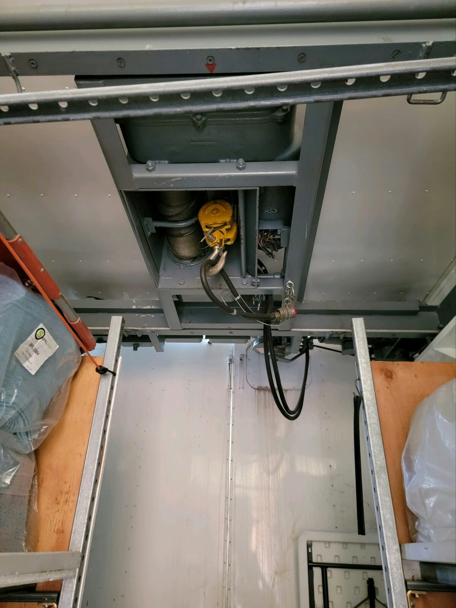 This image shows a ceiling-mounted winch with cables and hooks inside a storage space or vehicle.