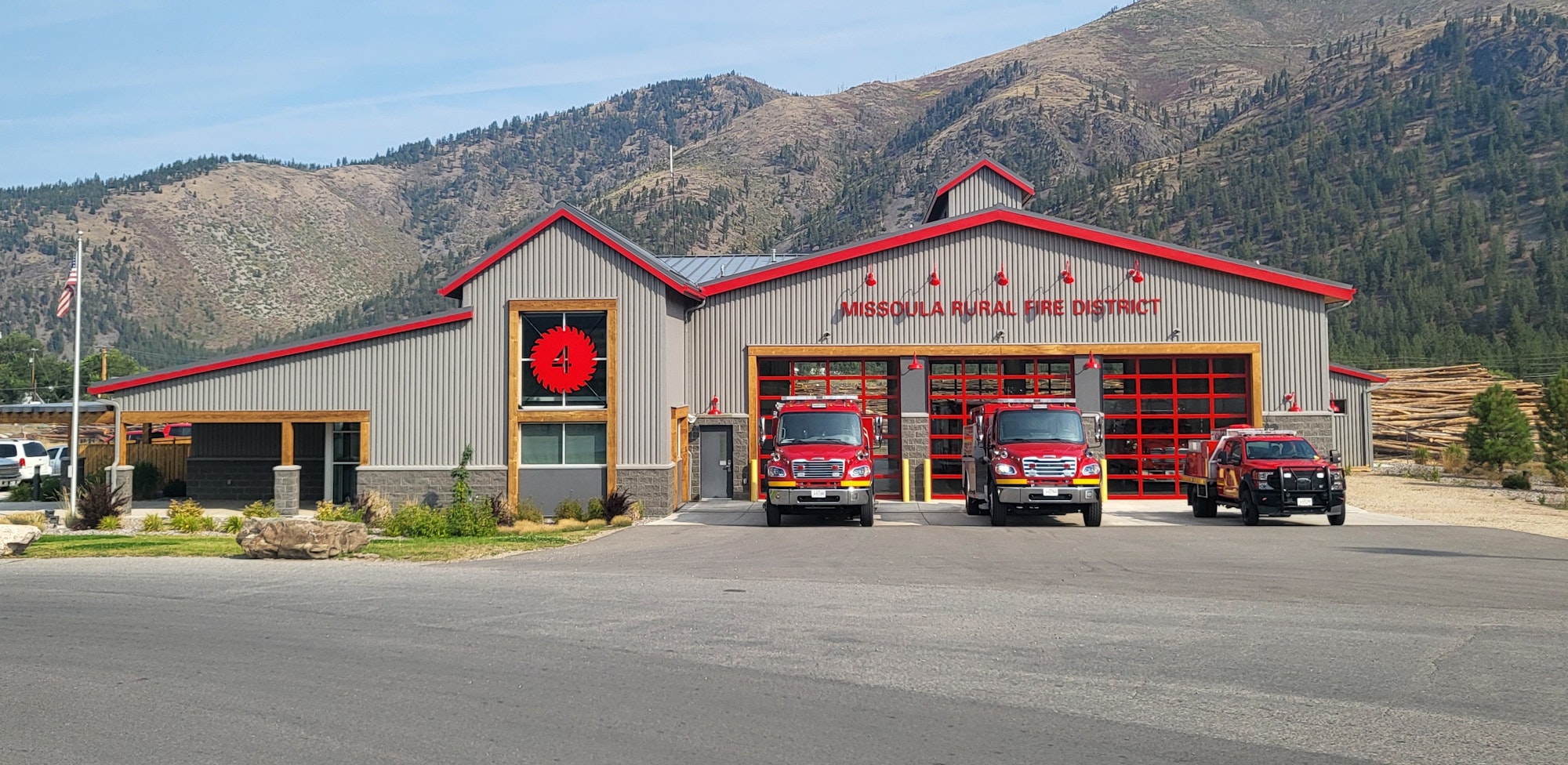 A fire station with a modern design, featuring red accents, two fire trucks in front, and mountains in the background.