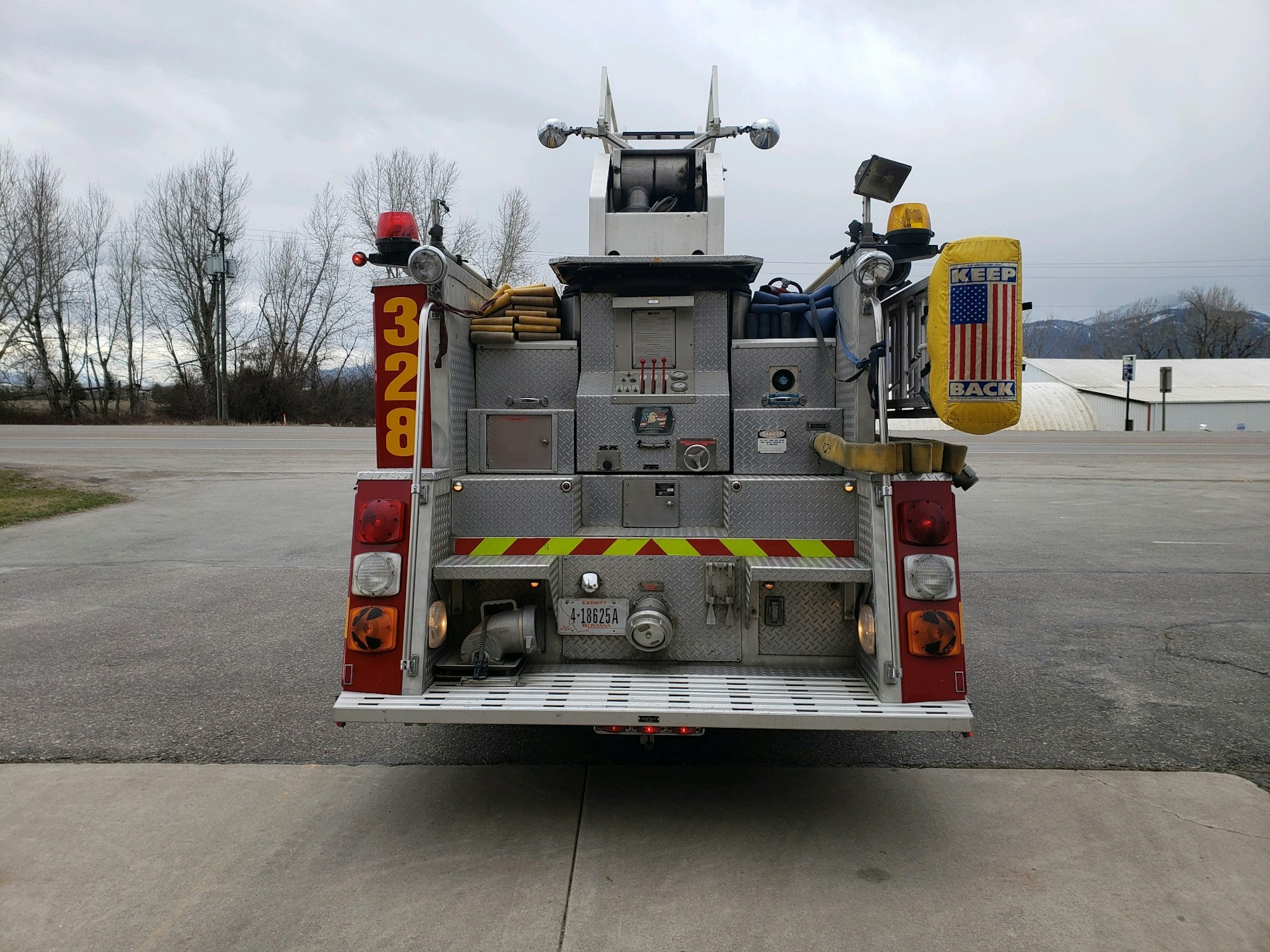 Rear view of a fire truck with equipment and a "Keep Back" sign on a city street.