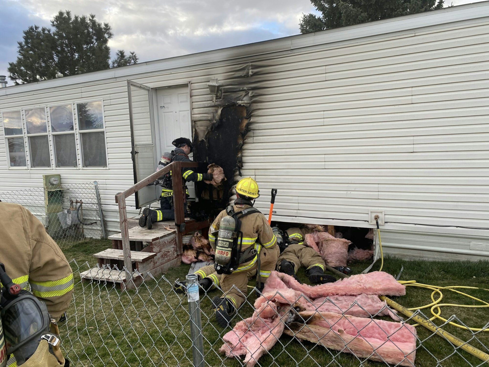 Firefighters responding to a house fire, assessing damage and removing insulation.