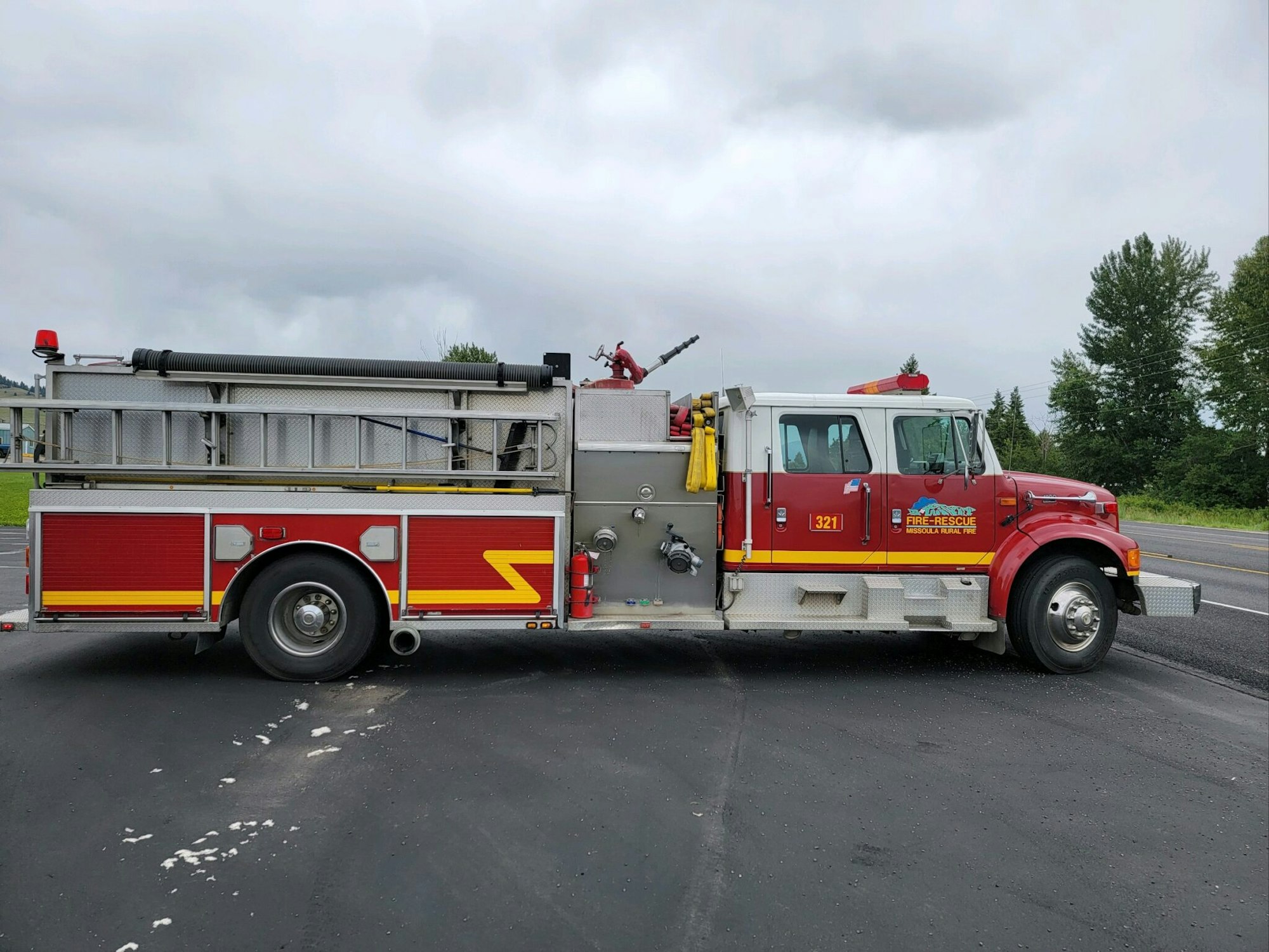 A red fire truck parked on an asphalt surface with trees in the background.