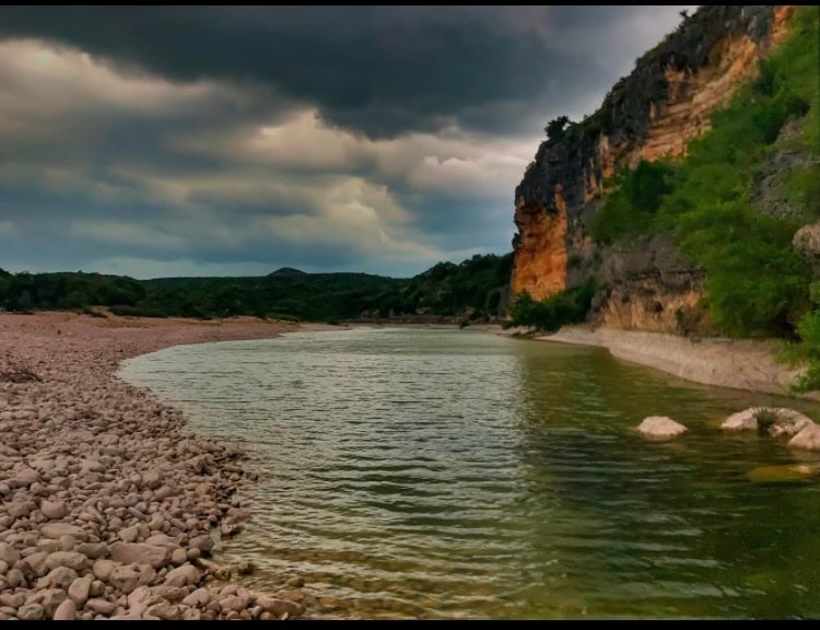 A river with rocky banks, cliffs, and overcast skies.