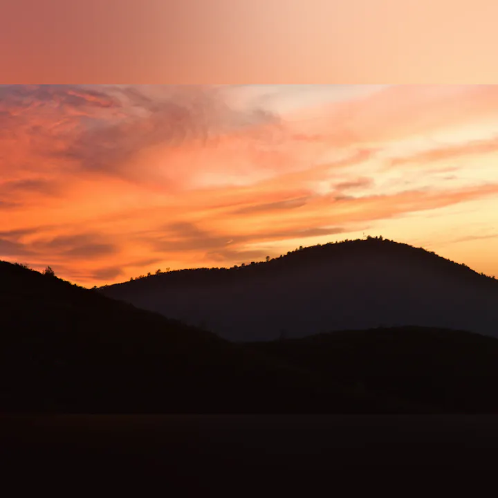 A stunning sunset over rolling hills, showcasing vibrant orange and pink hues in the sky.