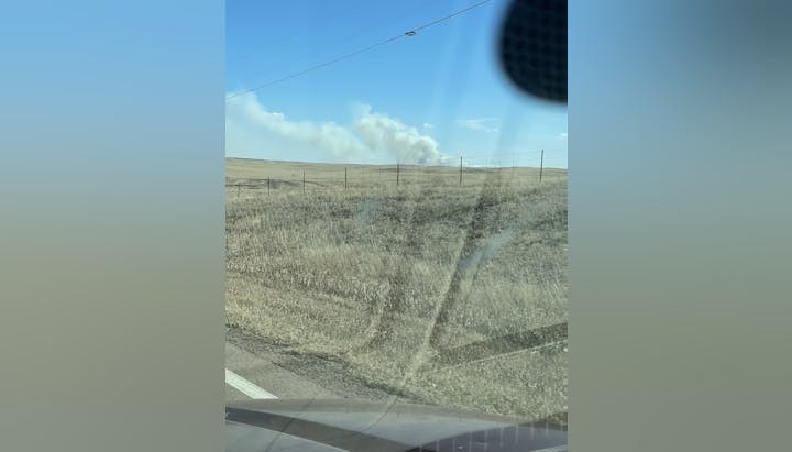 The image shows a vast landscape with smoke rising in the distance, possibly from a fire, under a clear blue sky.