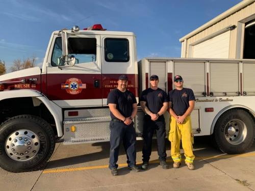 Three firefighters standing in front of a fire truck.