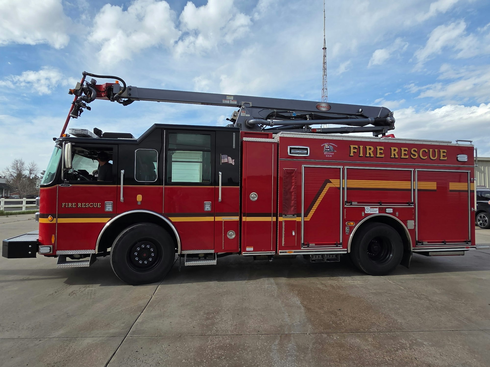 A fire rescue truck with an extendable ladder, parked on a concrete surface under a blue sky with clouds.