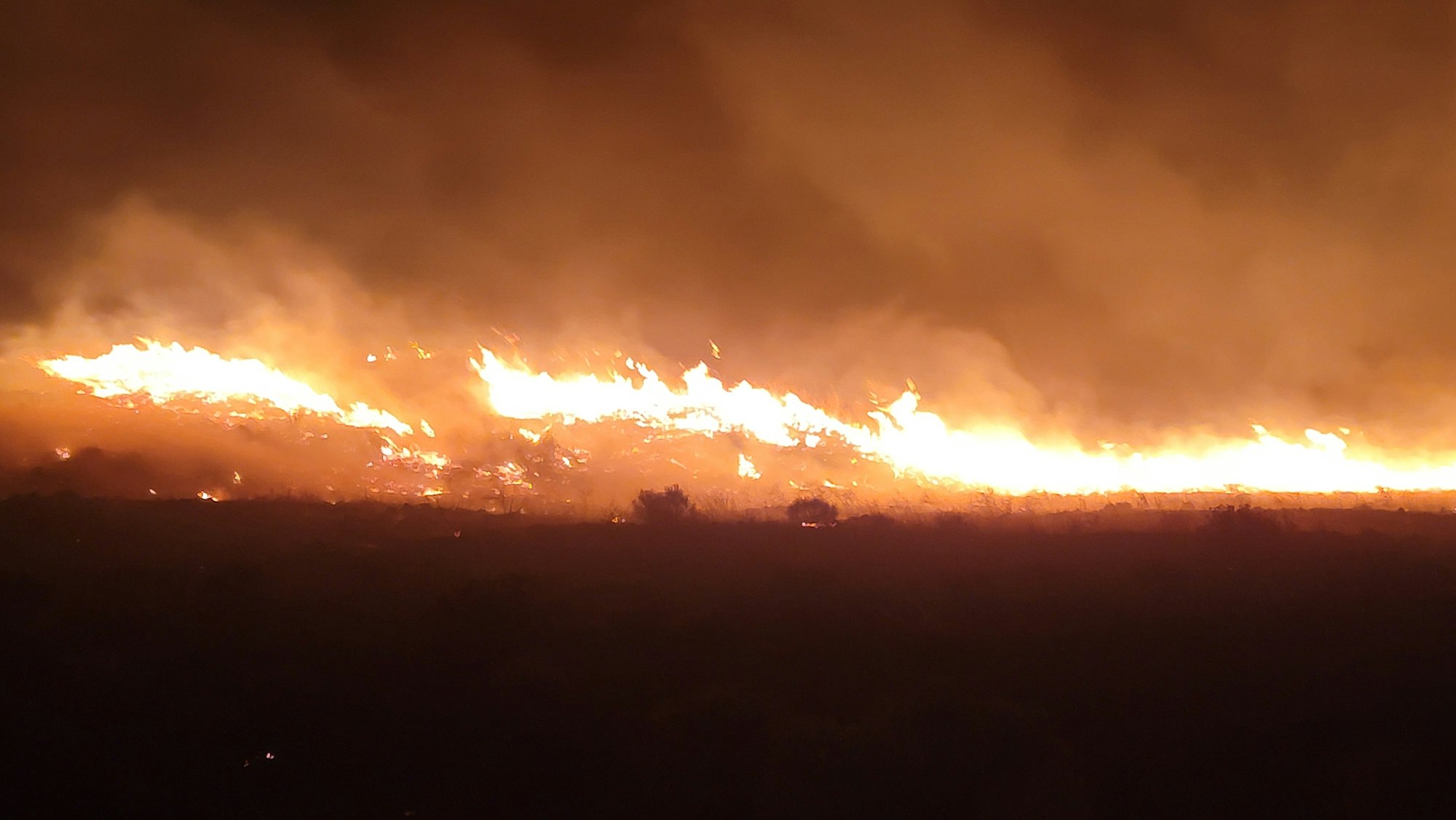 A large wildfire with intense flames and thick smoke at night.