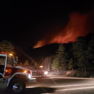Fire trucks near a forest fire at night.