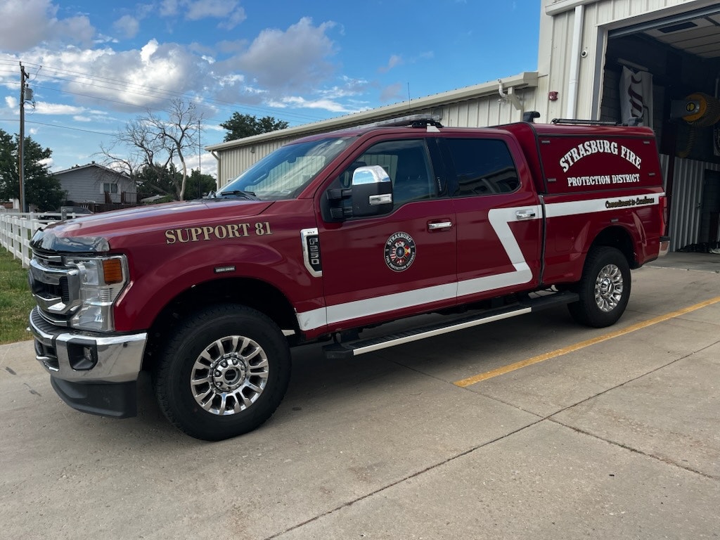 A red fire department support truck labeled "Strasburg Fire Protection District Support 81" parked outside a building.