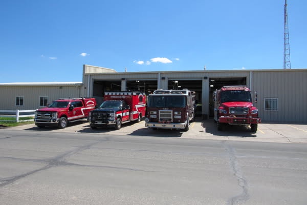 Fire station with four fire trucks parked in front of a garage under a clear blue sky.