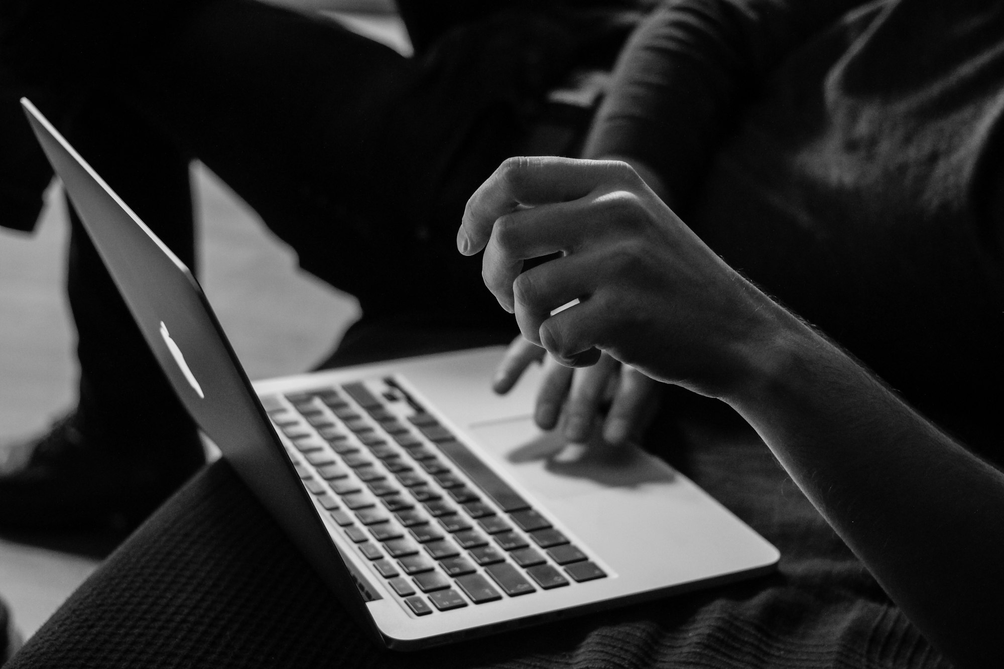 Person using a laptop, focusing on typing and gesturing with hands. Black and white image.