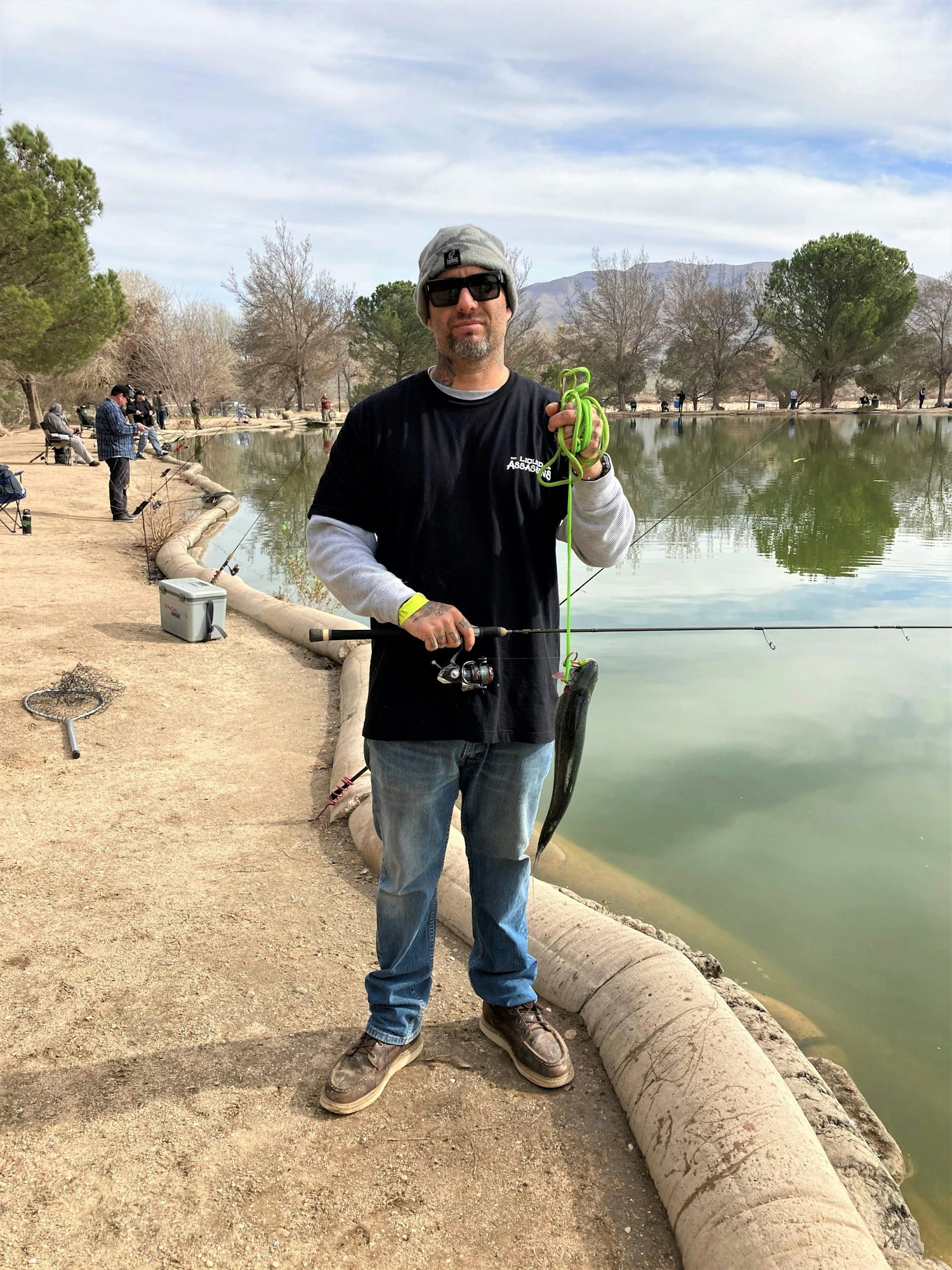 May contain: pants, clothing, pond, outdoors, nature, water, portrait, photography, person, head, face, park, grass, plant, jeans, scenery, tree, vegetation, soil, standing, glasses, accessories, man, adult, male, handbag, bag, baseball cap, hat, cap, and box