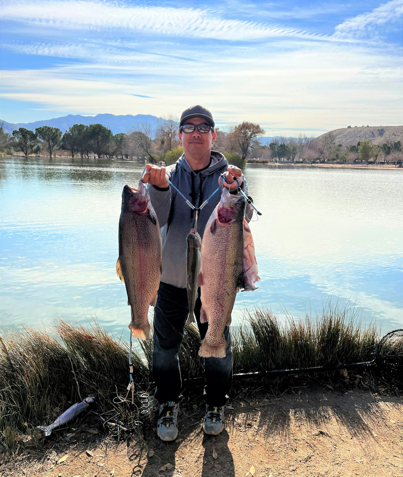 May contain: portrait, photography, person, head, face, soil, wilderness, outdoors, nature, lake, water, fishing, leisure activities, vegetation, plant, coho, fish, sea life, animal, pants, clothing, rock, mortar shell, weapon, glasses, accessories, jacket, coat, hat, tree, trout, shoe, footwear, and scenery