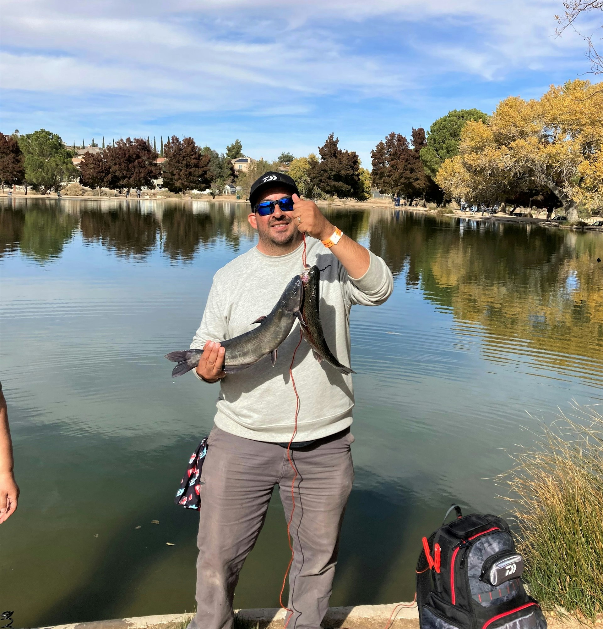 May contain: portrait, photography, person, head, face, pond, outdoors, water, nature, tree, plant, vegetation, fishing, leisure activities, lake, hat, clothing, rock, grass, scenery, man, adult, male, glasses, accessories, waterfront, trout, fish, sea life, animal, sunglasses, bracelet, jewelry, shoe, footwear, wilderness, and pants