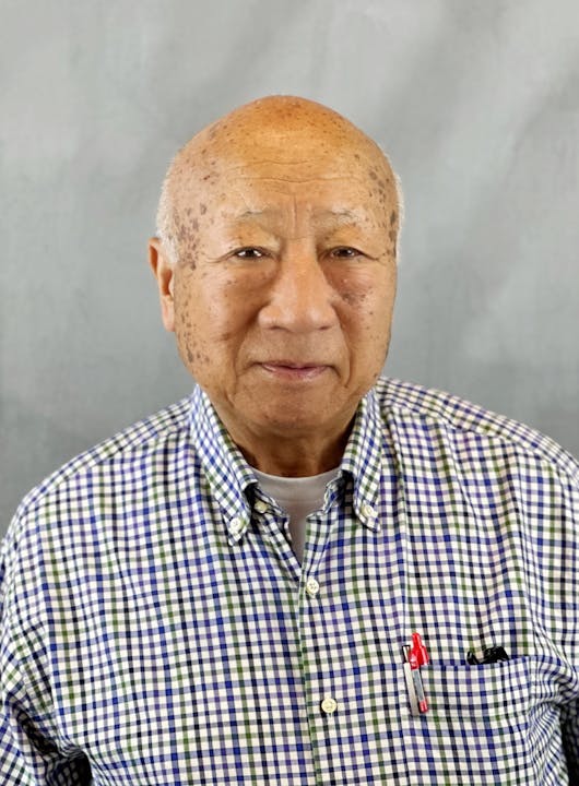 An older person with a checkered shirt and pens in a pocket.