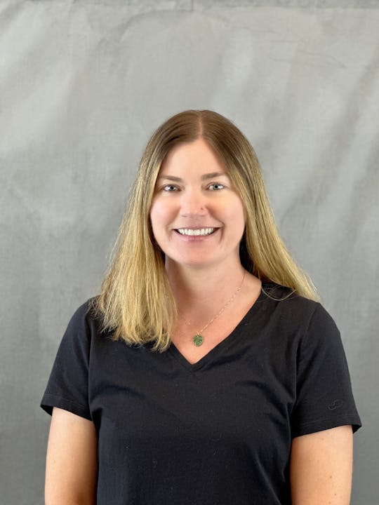 A smiling person with a black shirt against a grey backdrop.