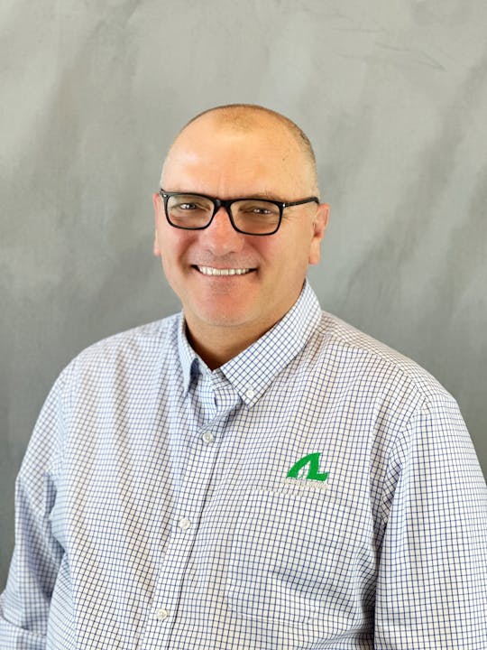 A smiling person with glasses wearing a checkered shirt with a logo.