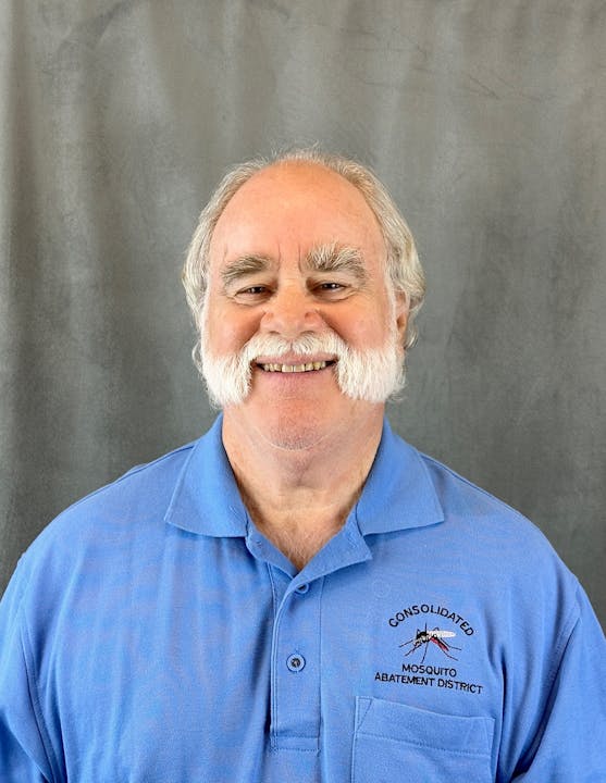 A smiling man in a blue shirt with an embroidered logo: "Consolidated Mosquito Abatement District." Gray background.