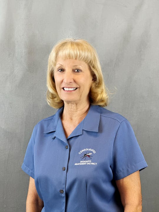A smiling woman in a blue work shirt with a mosquito graphic and text emblem.