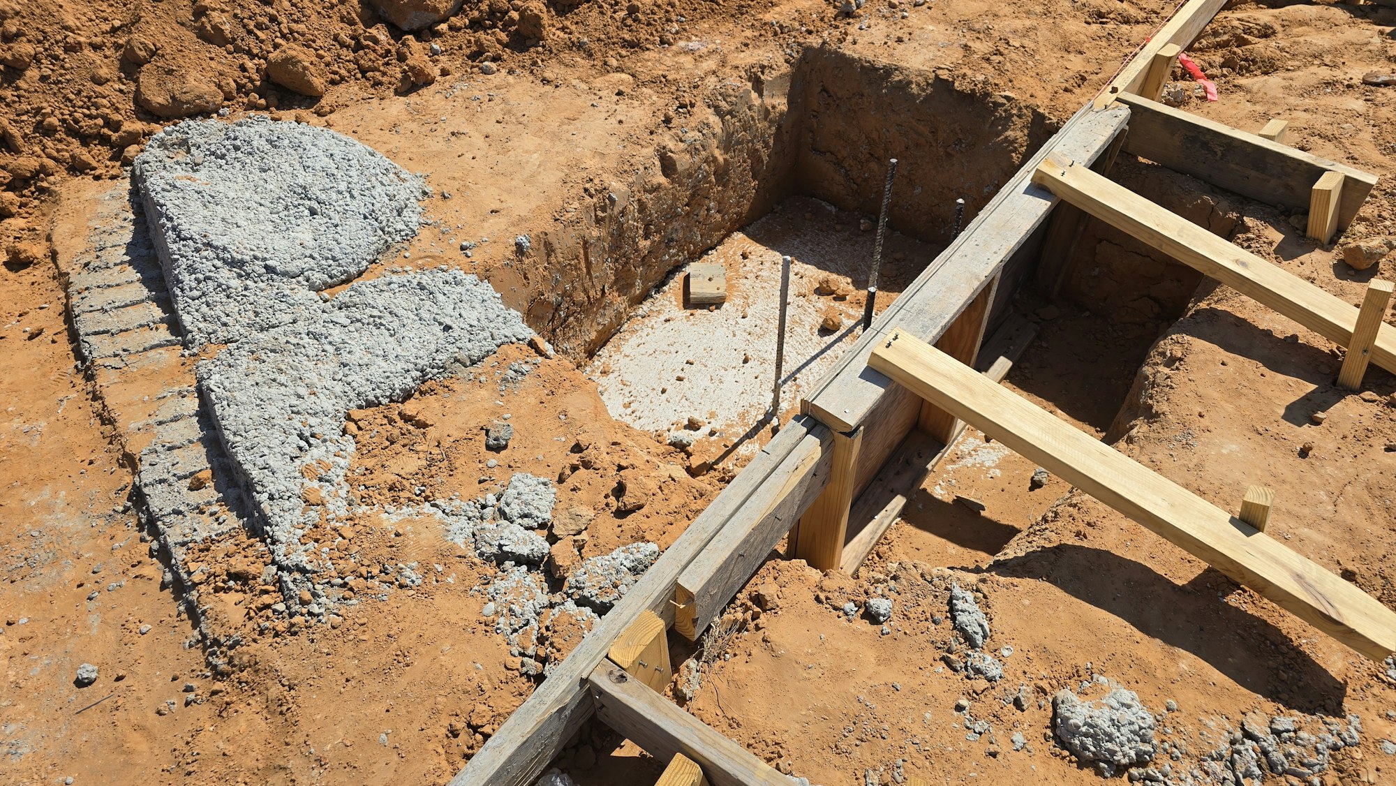 The image shows an excavation site with concrete, dirt, and wooden supports indicating preparation for construction.