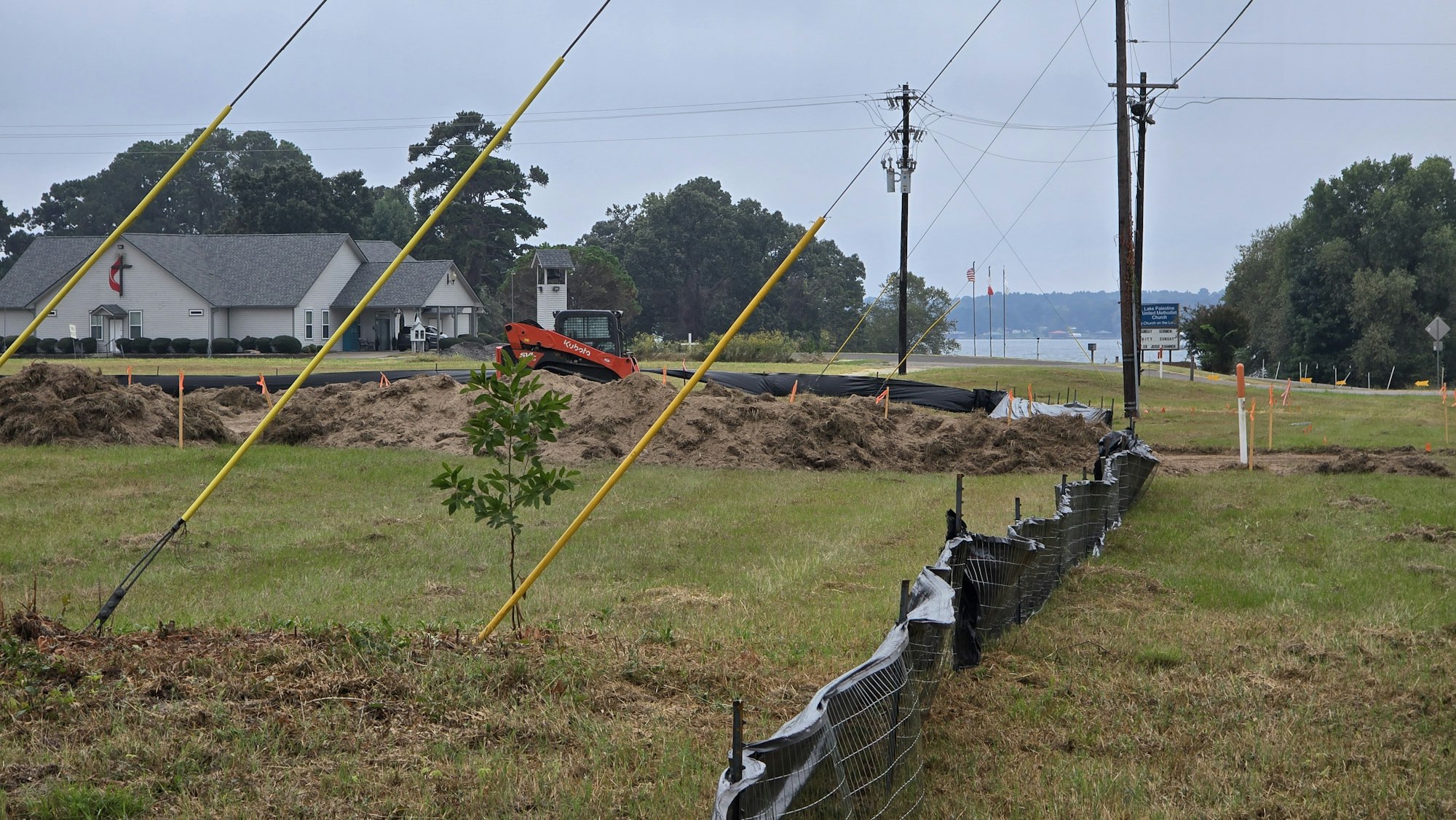 A church, construction site with a small vehicle, utility poles, and a fenced grassy area.