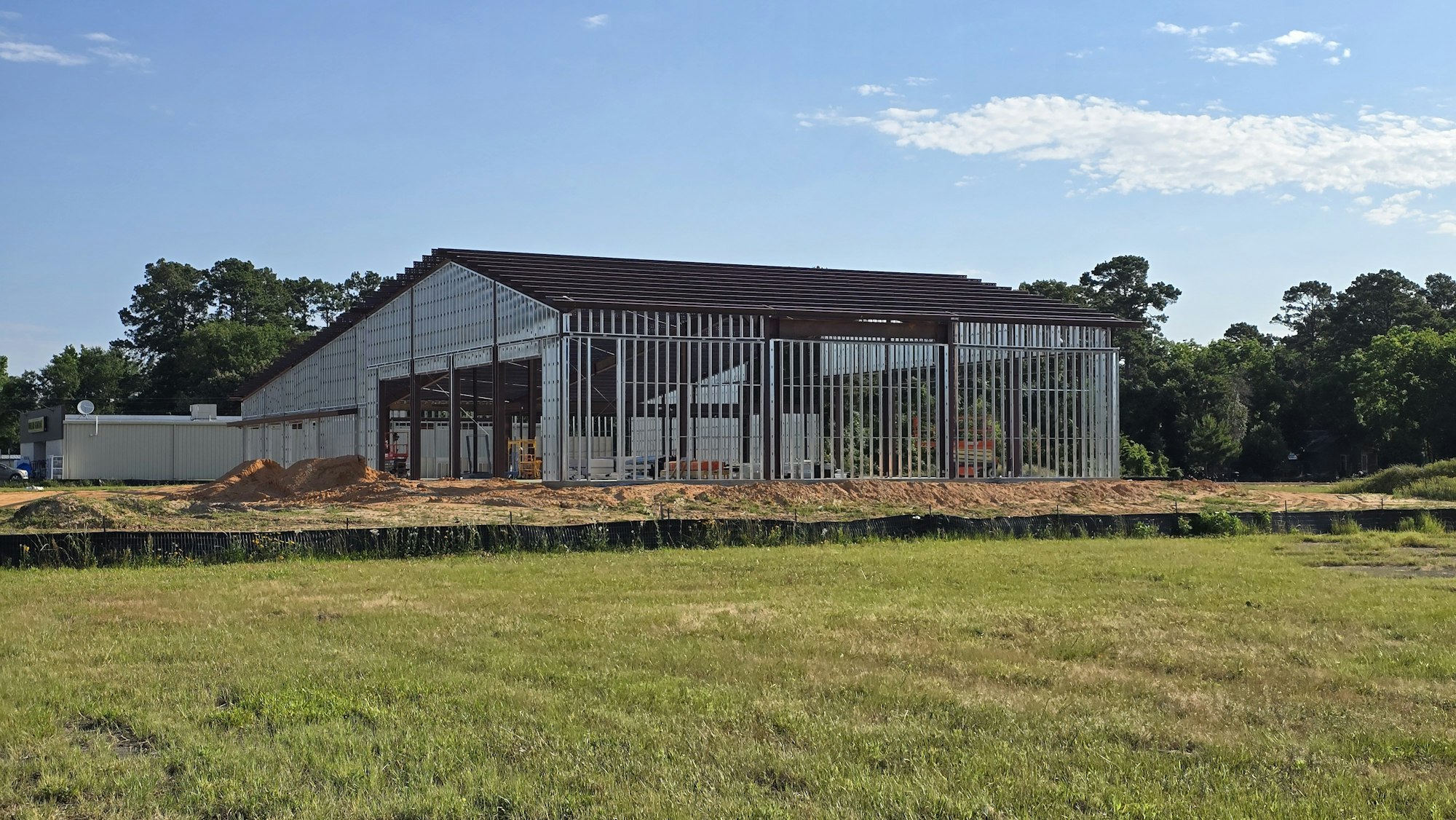 A partially constructed metal building on a grassy lot, with clear blue skies and trees in the background.