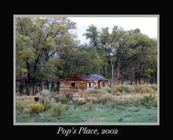 A rustic cabin in a wooded area labeled "Pop's Place, 2002" with trees and grassy surroundings.
