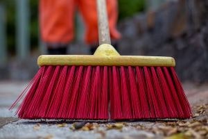 A red broom sweeping leaves on a paved surface.