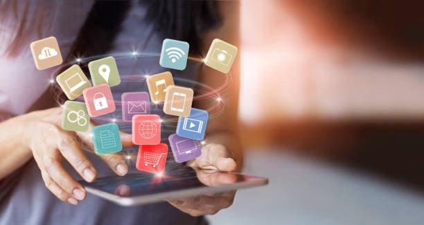 A person using a tablet with colorful app icons floating above it, representing digital and technology concepts.