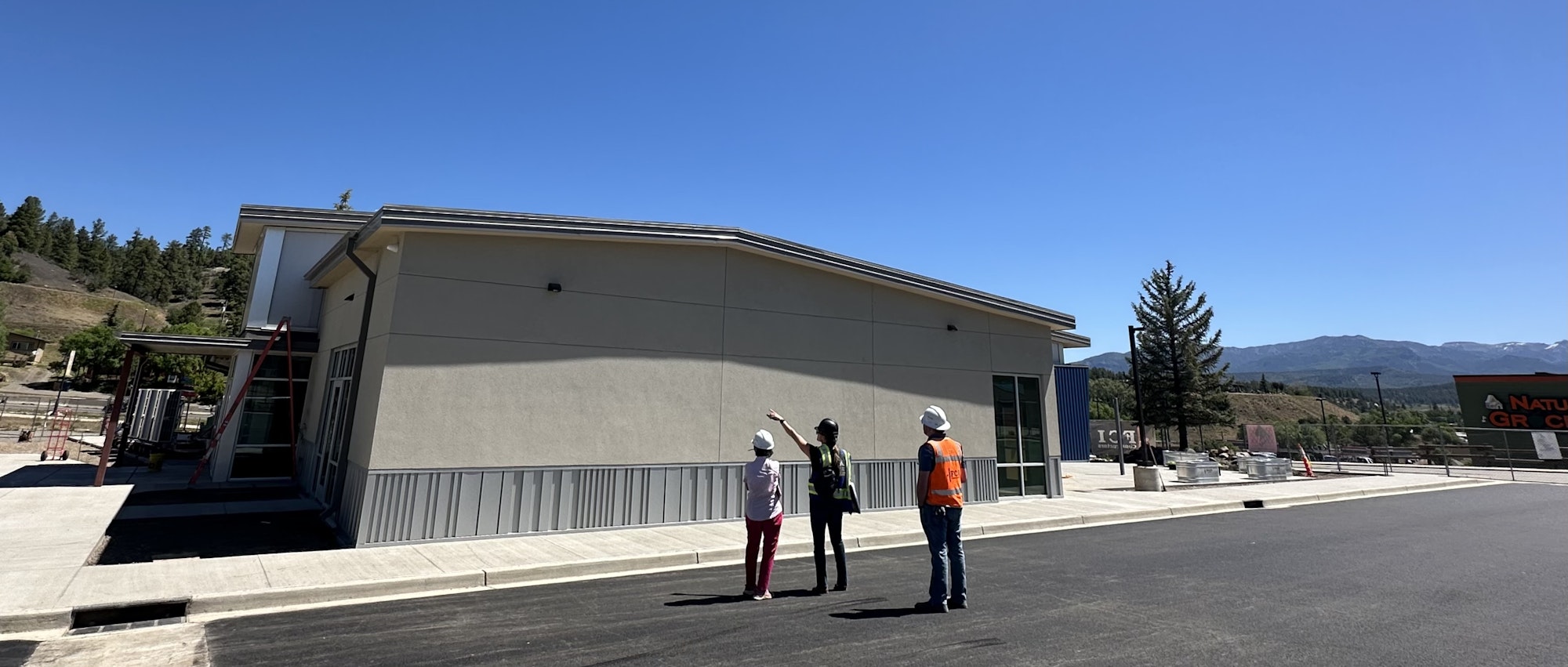 A group of people in hard hats inspects a building under a clear blue sky, discussing features and construction elements.