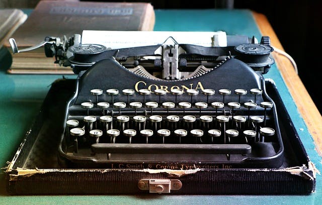 A vintage Corona typewriter on a desk with a book in the background.