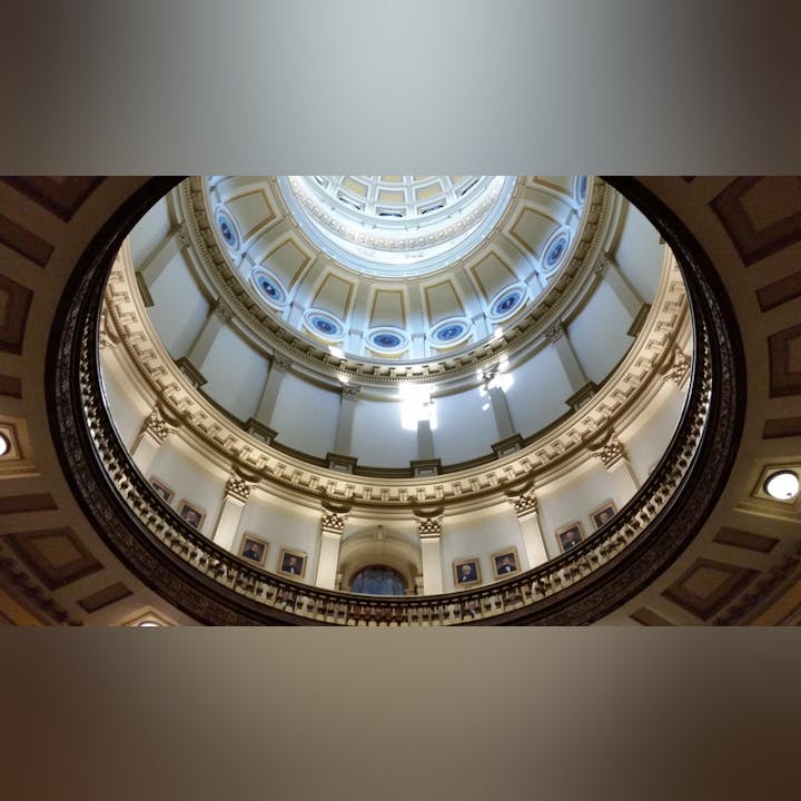 Ornate dome interior with columns and framed portraits, viewed from below.