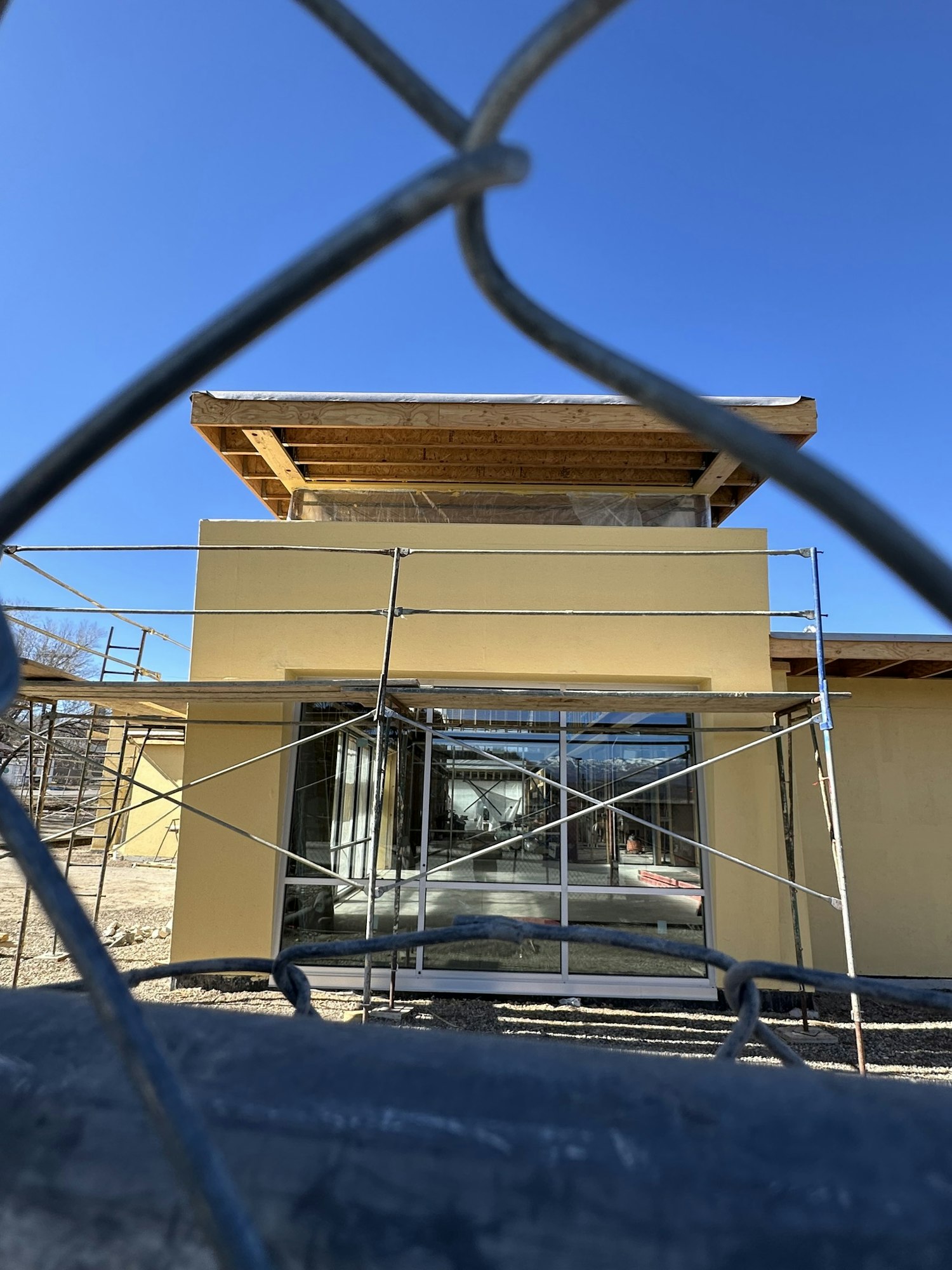 The image shows a construction site with a yellow building, scaffolding, and a bright blue sky in the background.