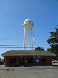 A water tower standing above a single-story building against a clear blue sky.