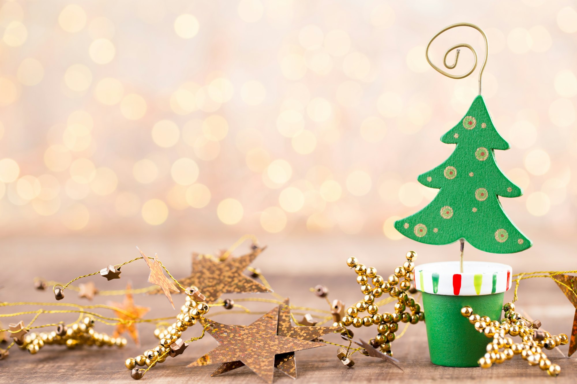 A small decorative green Christmas tree in a pot, surrounded by gold star garlands and soft bokeh lights in the background.